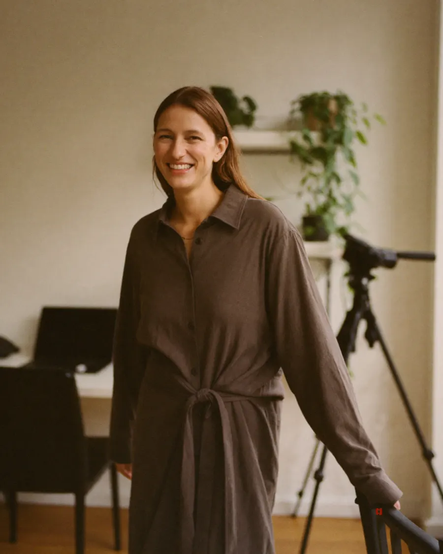 A creator standing in her studio, smiling, a camera on a tripod behind her.